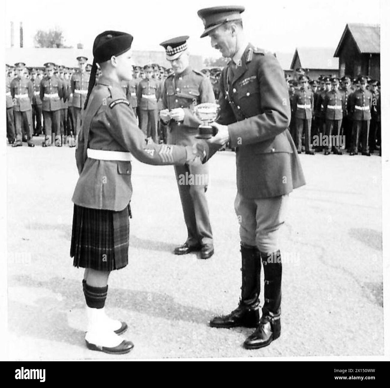 Le major général R. Evans remet une coupe à A. Cunningham dans une école technique pour garçons de Stirling pour avoir remporté un concours de danse des Highlands, soulignant la reconnaissance formelle et la pratique cérémonielle. Banque D'Images