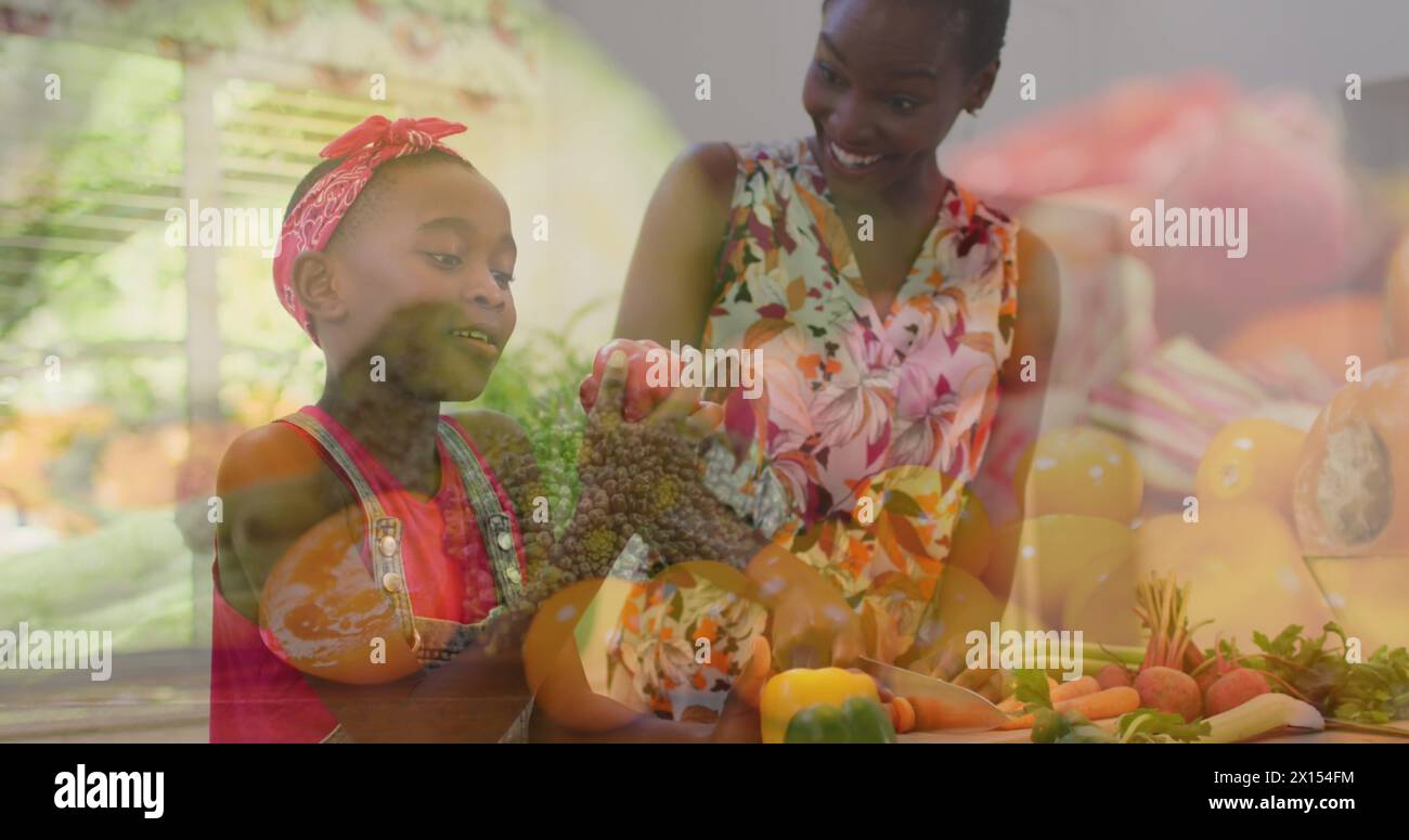 Image composite de légumes contre mère et fille afro-américaine cueillant des légumes Banque D'Images