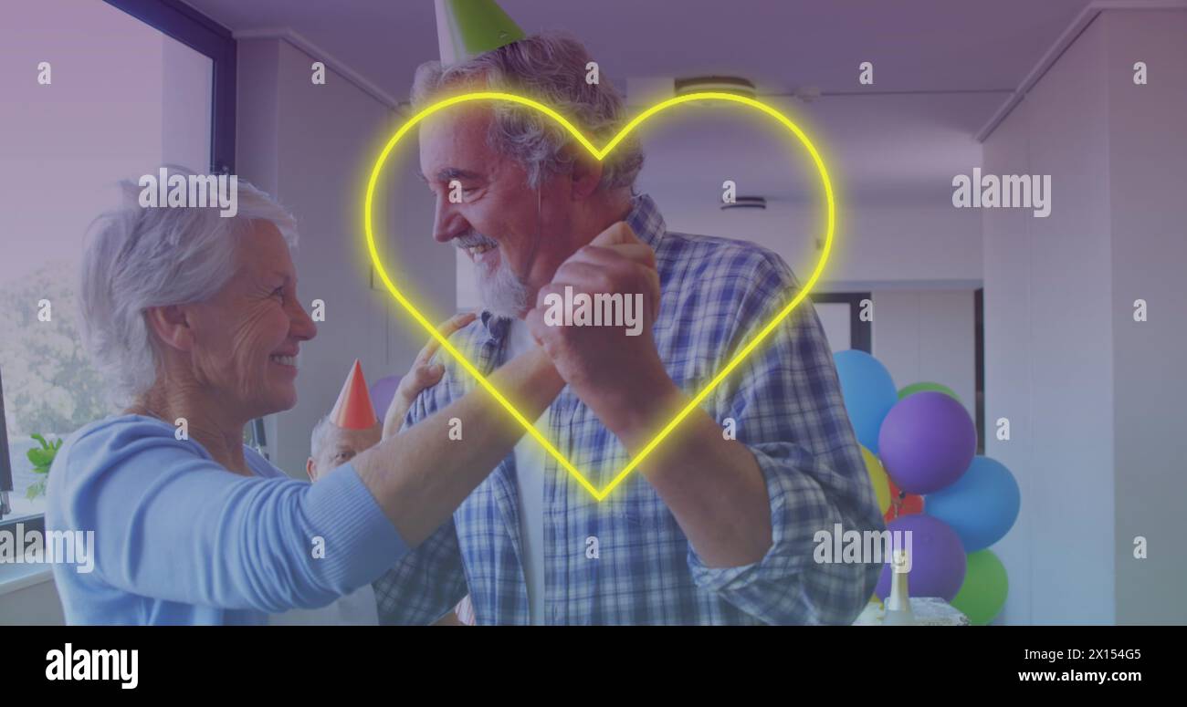 Icône de coeur de néon jaune contre un couple de personnes âgées caucasiennes dansant ensemble pendant la fête d'anniversaire Banque D'Images