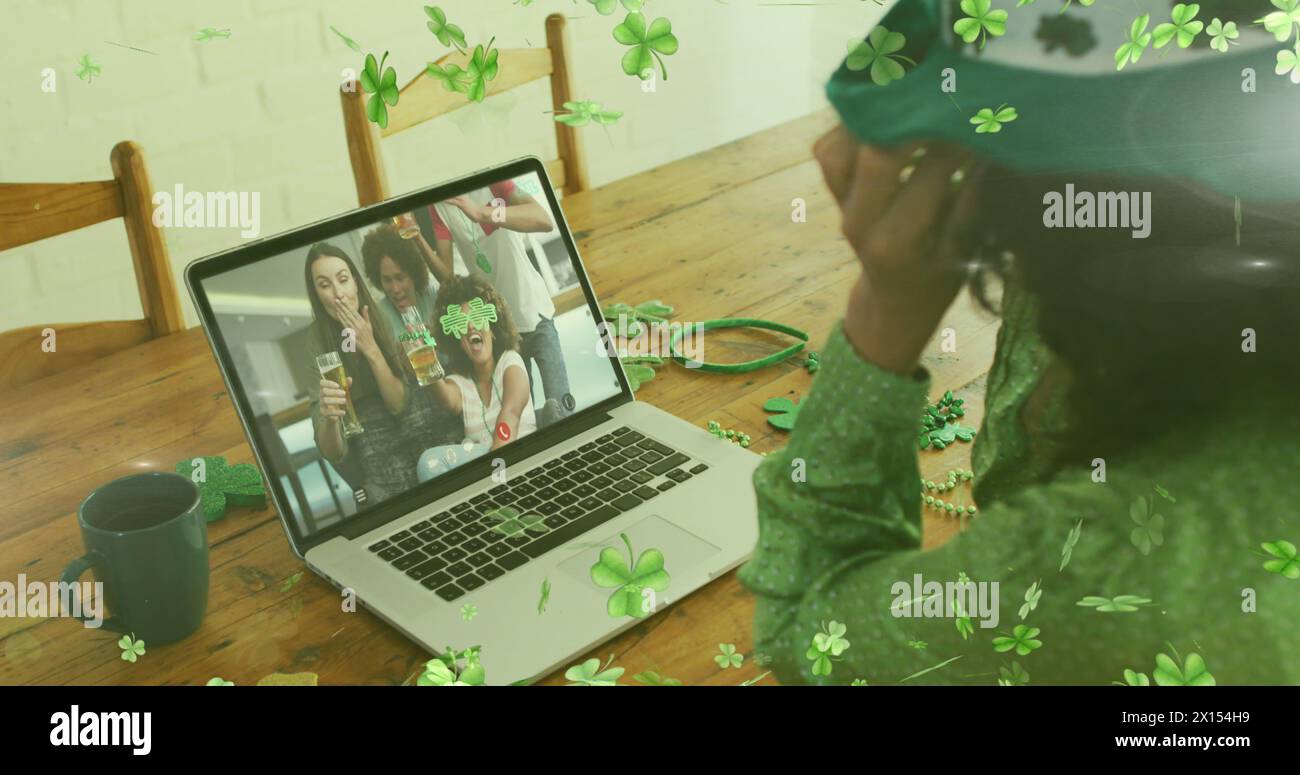Image de feuilles de trèfle au-dessus d'une femme célébrant la fête de St patrick avec des amis sur l'appel d'image d'ordinateur portable Banque D'Images