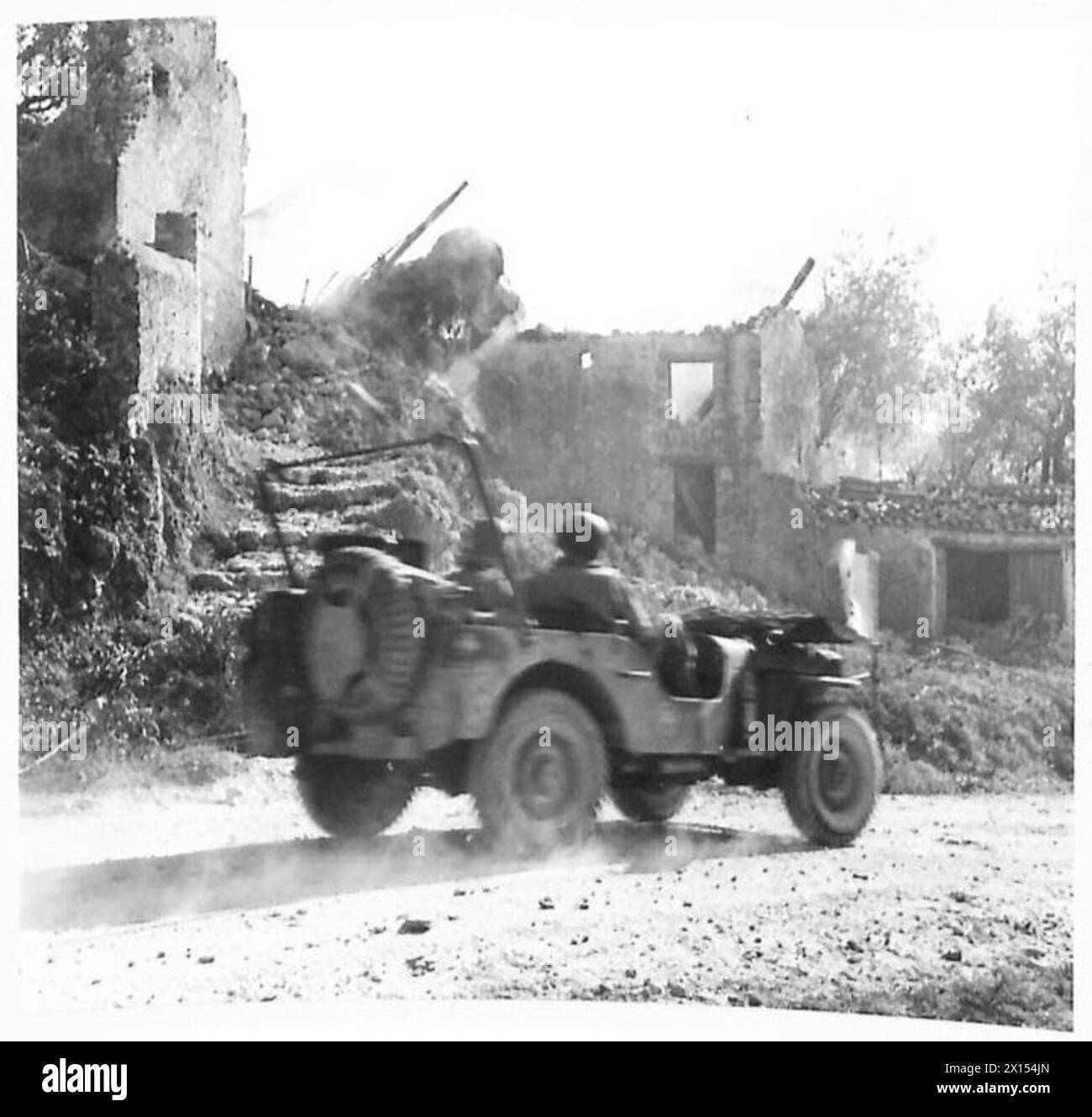 Une Jeep de l'armée britannique passe devant des maisons incendiées par des bombardiers en piqué ennemis dans le secteur américain du front de la cinquième armée en Italie. Banque D'Images