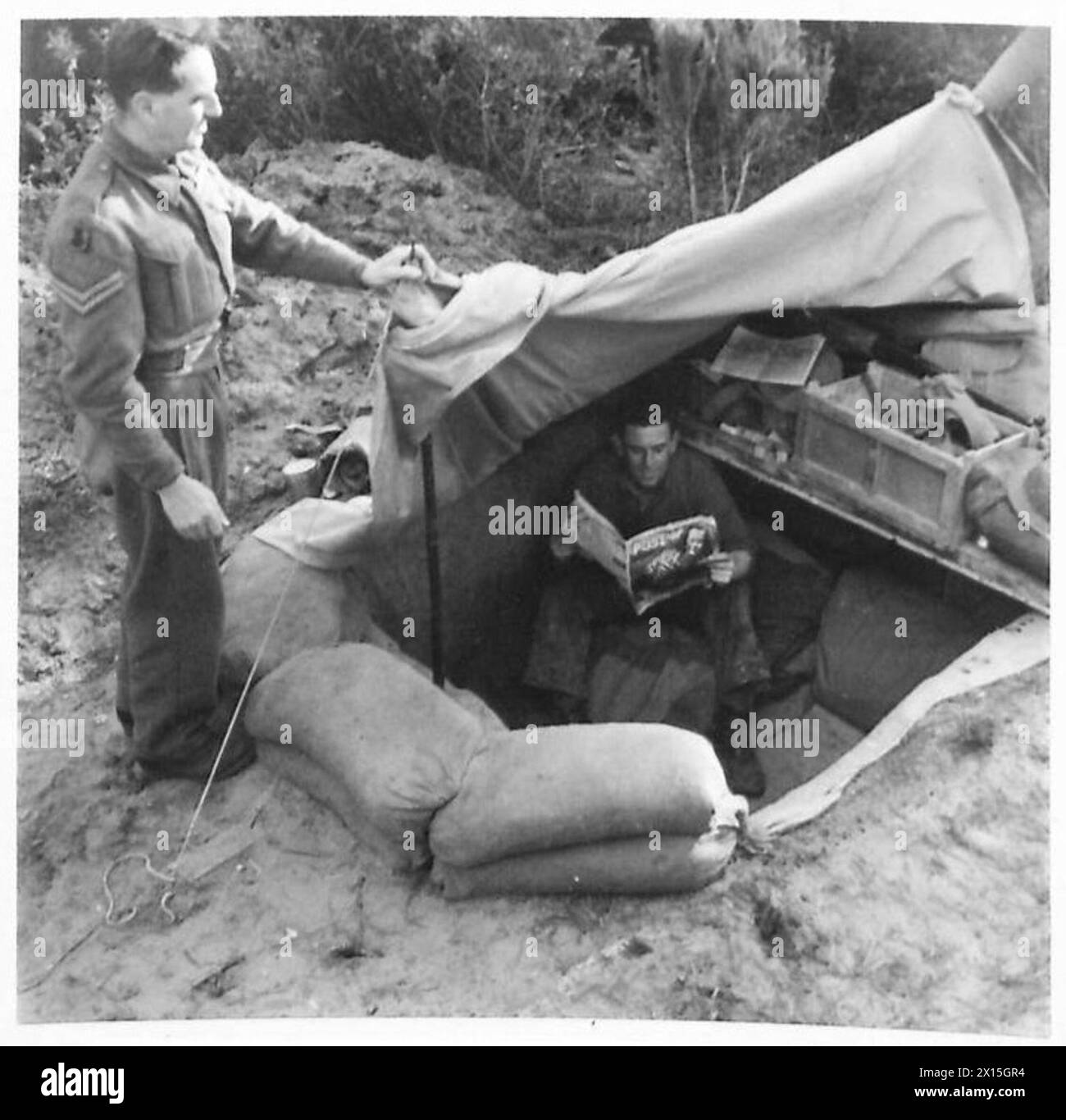 À la tête de pont d’Anzio, le Cpl Bamber lève le flanc de son bivouac pour révéler le l/Cpl. Hicks à l'intérieur, avec plancher de tente et côtés doublés de sac et de bois pour le stockage et la protection du kit. Banque D'Images