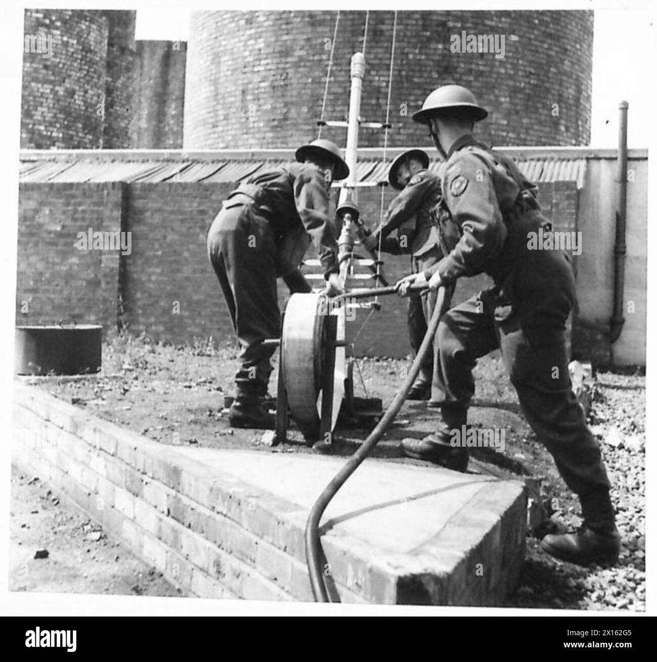 Les pompiers de l'armée positionnent un tuyau d'embranchement de fabrication de mousse pour combattre un incendie de char élevé, connectant le tuyau de mousse au tuyau pour les opérations de lutte contre l'incendie. Banque D'Images