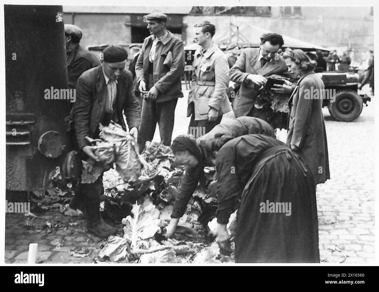 Les habitants locaux visitent un marché pour acheter des produits verts frais, observés par les forces britanniques. Banque D'Images