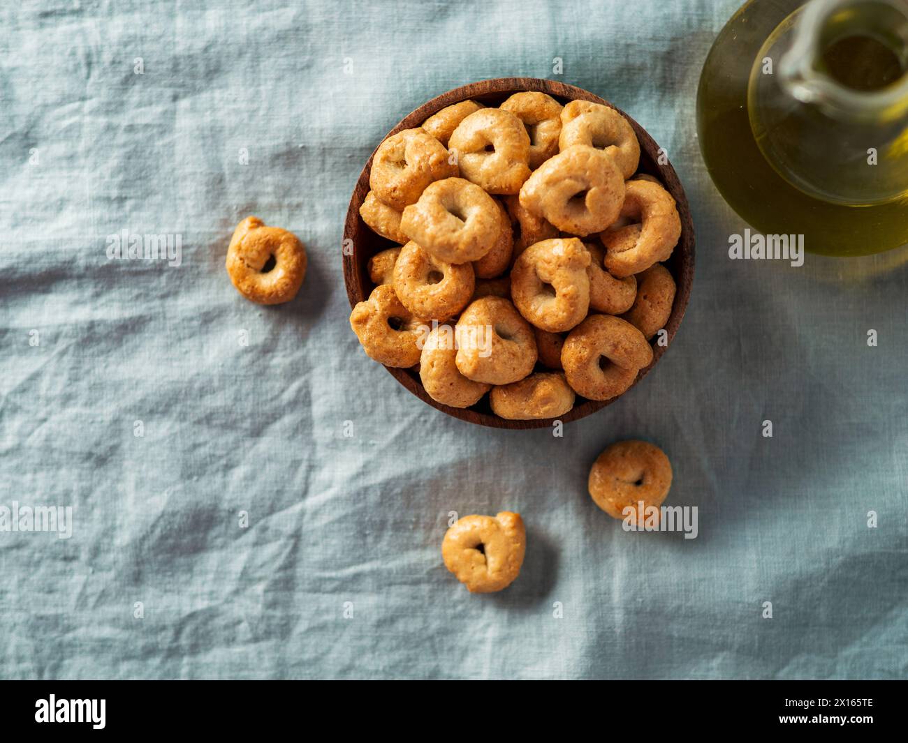 Taralli ou tarallini italien traditionnel dans un bol en bois sur fond de serviette en lin bleu clair. Coup rustique de taralli hors-d'œuvre avec espace de copie. Vue de dessus ou à plat. Banque D'Images