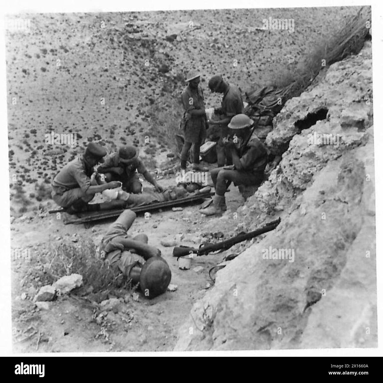 Au cours d'une patrouille à l'aube à Tobrouk, l'officier de patrouille s'occupe d'une victime tandis que d'autres membres se reposent pour fumer et boire pendant un arrêt temporaire. Banque D'Images