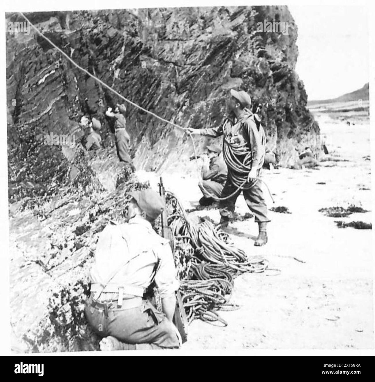 Les membres des Green Devils versent de la corde d'une plage tandis que le premier soldat grimpe sur des rochers pendant l'entraînement de l'armée britannique. Banque D'Images
