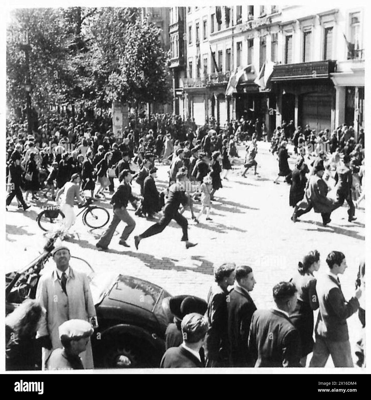 Les avions allemands survolent une ville alors que le Palais de Justice est incendié. Les civils courent pour s'abriter pendant que le personnel de l'armée britannique observe. Banque D'Images