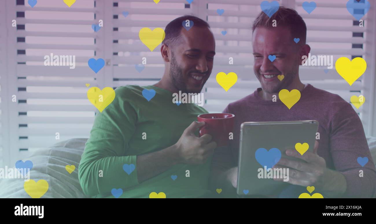 Image de cœurs sur un couple gay diversifié souriant et utilisant la tablette Banque D'Images