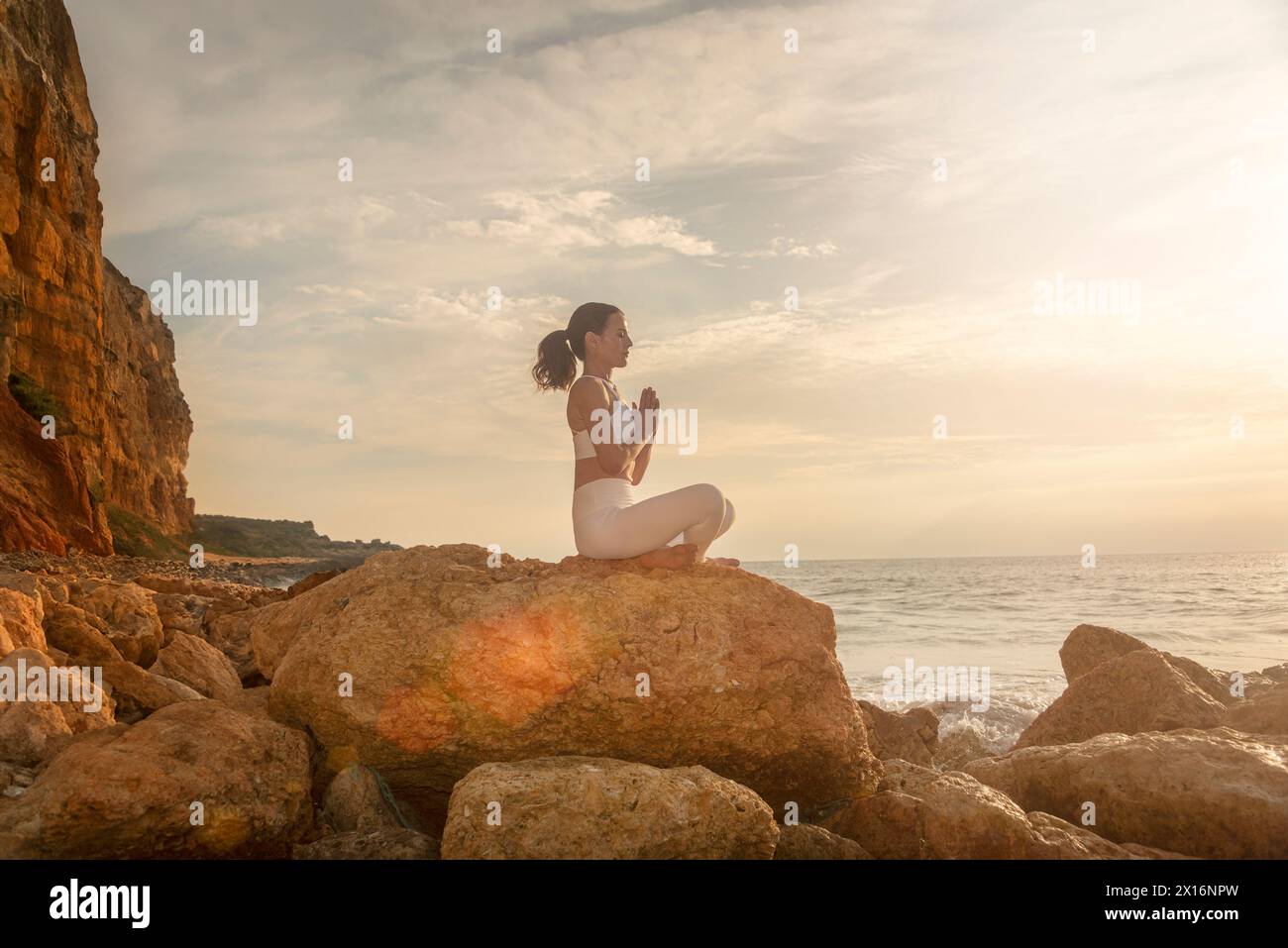 femme sportive pratiquant le yoga et méditant sur les rochers au bord de la mer au lever ou au coucher du soleil. Banque D'Images