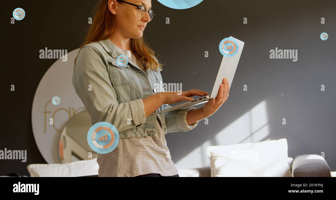 Image de plusieurs icônes graphiques sur une femme caucasienne debout et utilisant un ordinateur portable dans le bureau Banque D'Images