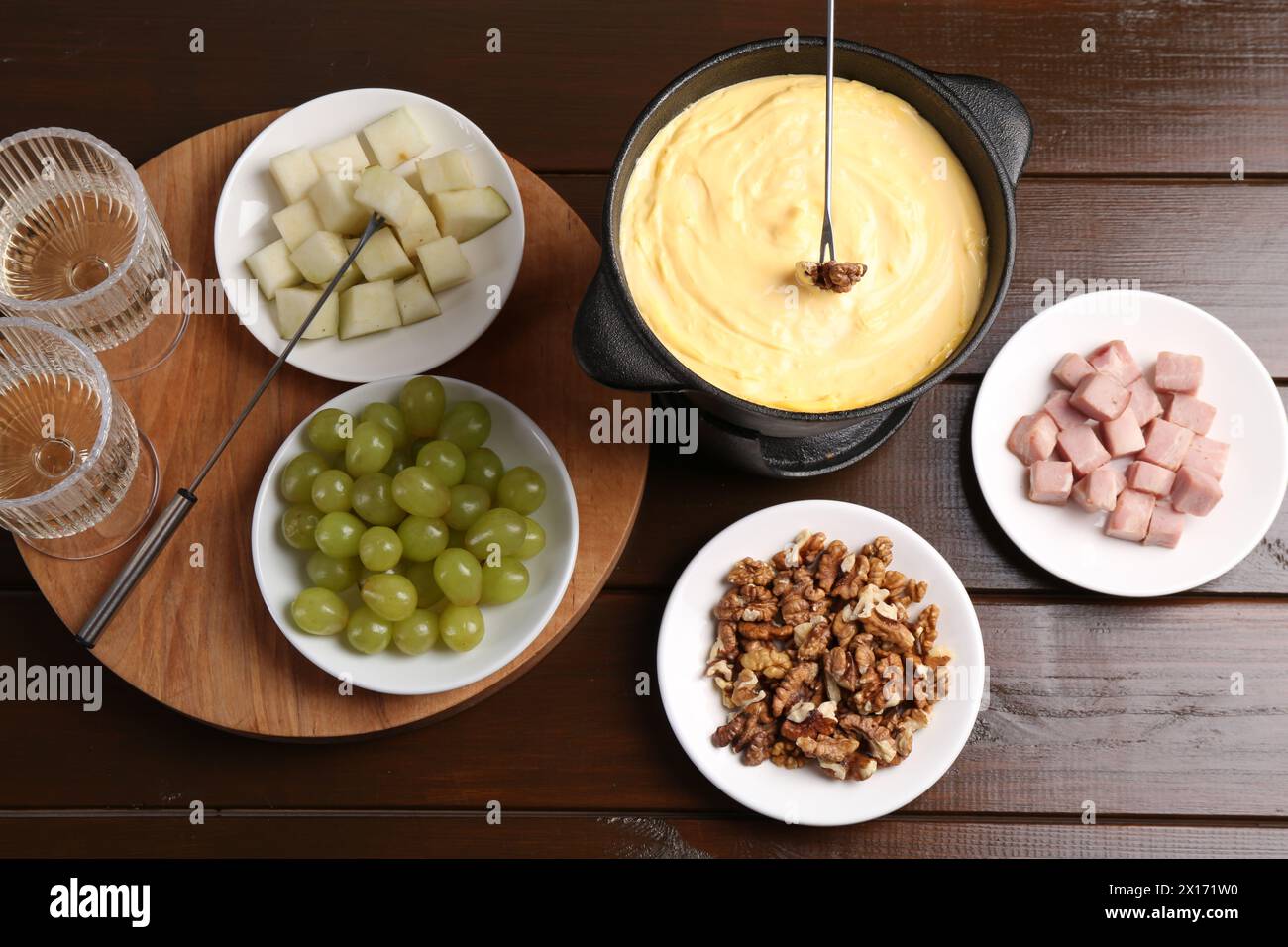 Pot à fondue avec fromage fondu savoureux, fourchettes, vin et différentes collations sur table en bois, plat Banque D'Images