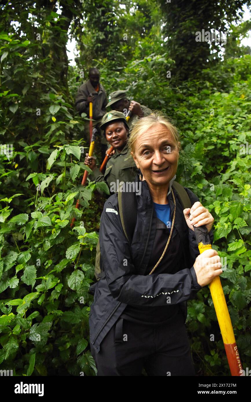 Au milieu d'une végétation dense, une femme européenne, pleine d'anticipation, marche aux côtés du directeur du parc et de son assistant dans le Bwindi National par en Ouganda Banque D'Images