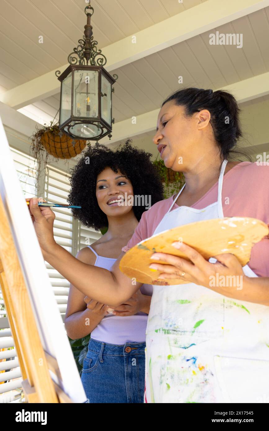 Mère biraciale et fille adulte peignant ensemble à la maison, mère tenant la palette Banque D'Images