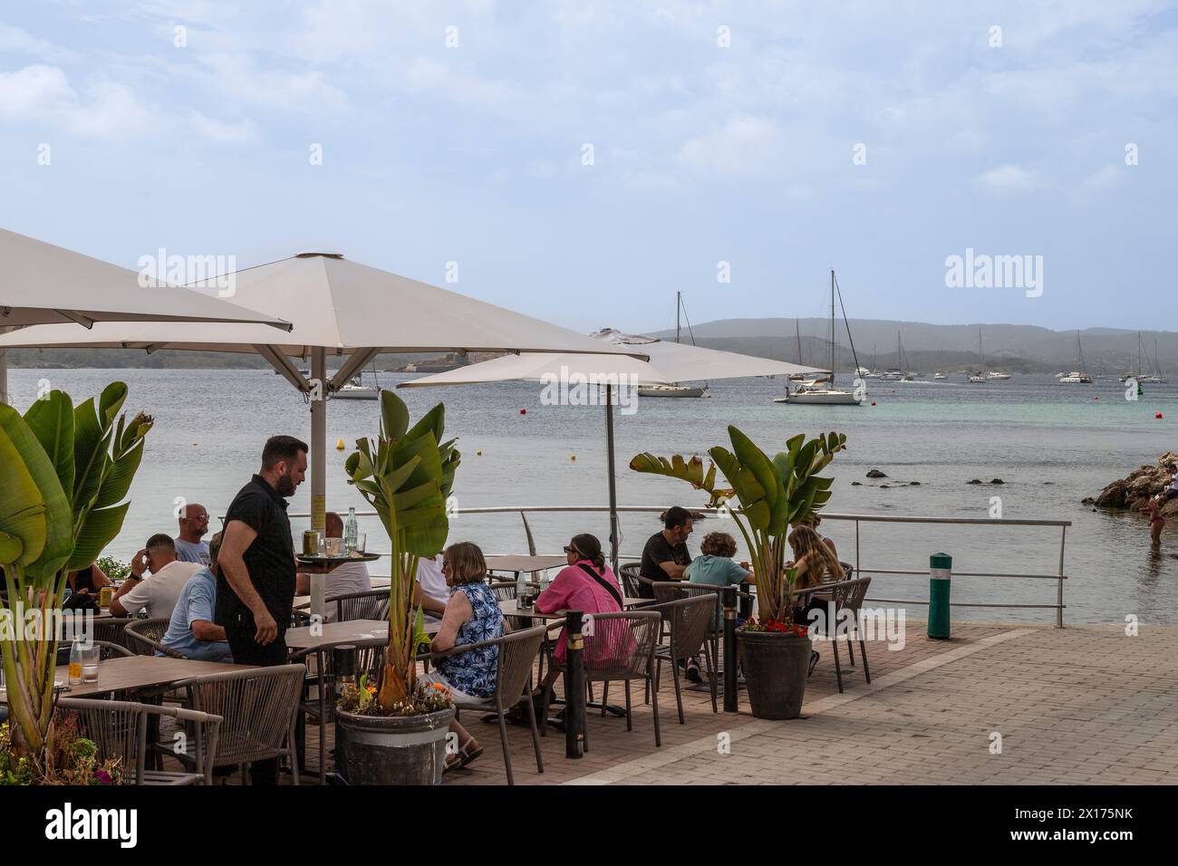 Les gens apprécient la terrasse le long de la baie dans la ville côtière de Fornells, Minorque. Banque D'Images