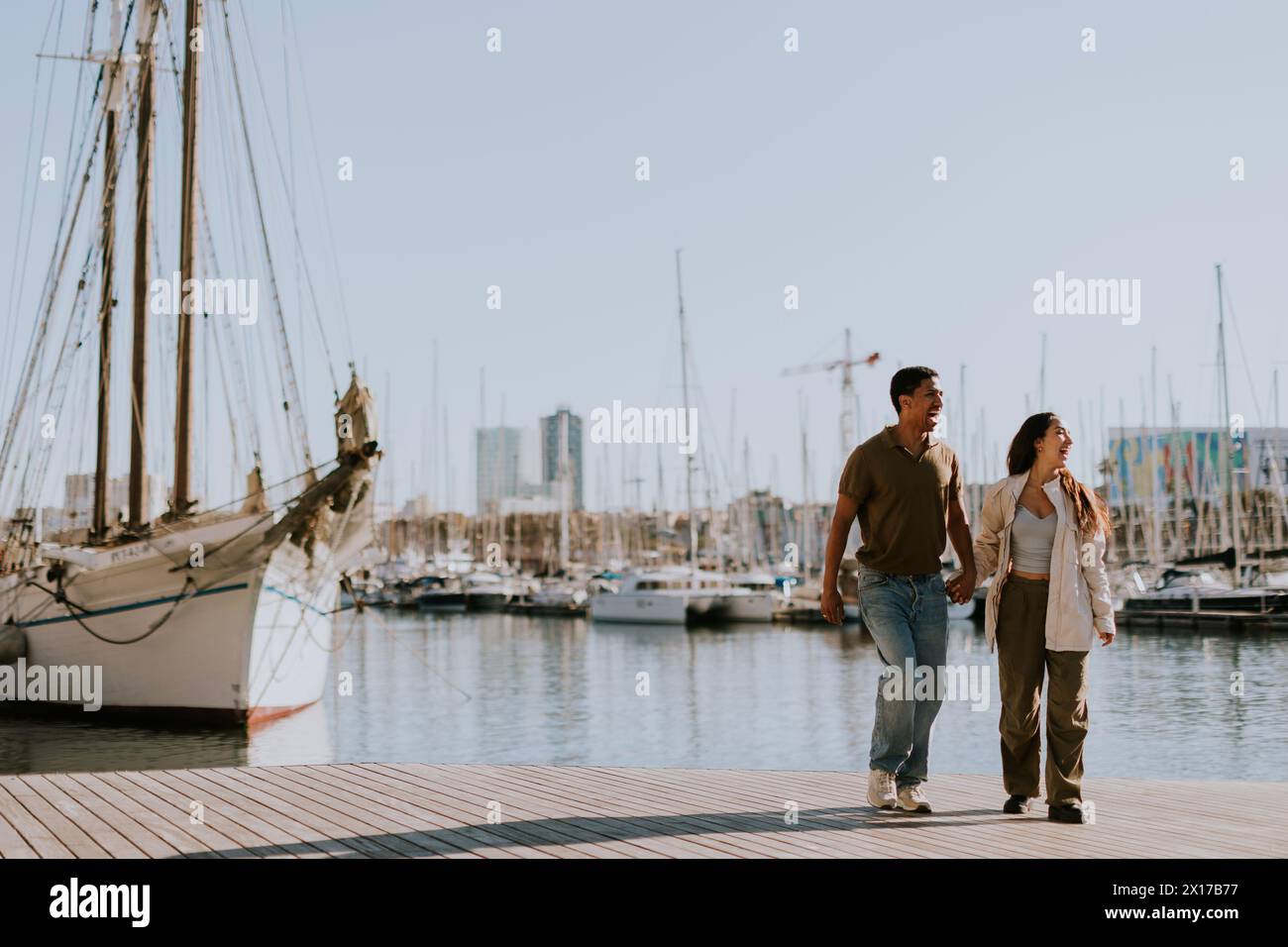 Cuple profite d'une promenade paisible à côté de bateaux amarrés dans la marina tranquille de Barcelone, se prélasser dans la douce lumière du matin. Banque D'Images