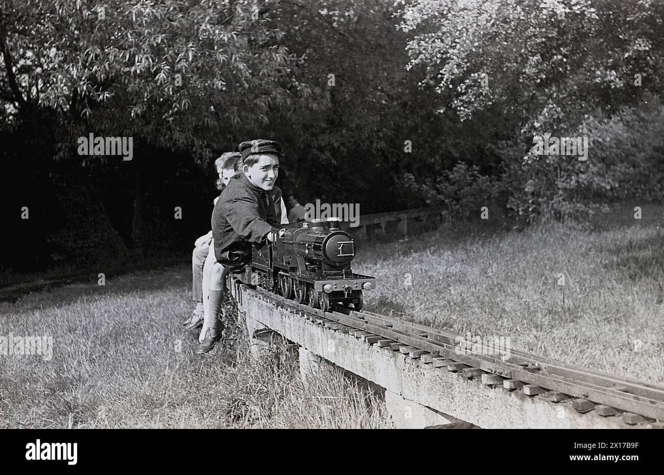 Années 1970, historique, été et à l'extérieur dans un champ, sur une voie ferrée surélevée, un conducteur de train donnant aux enfants un tour sur un chemin de fer à vapeur miniature, Angleterre, Royaume-Uni. Banque D'Images