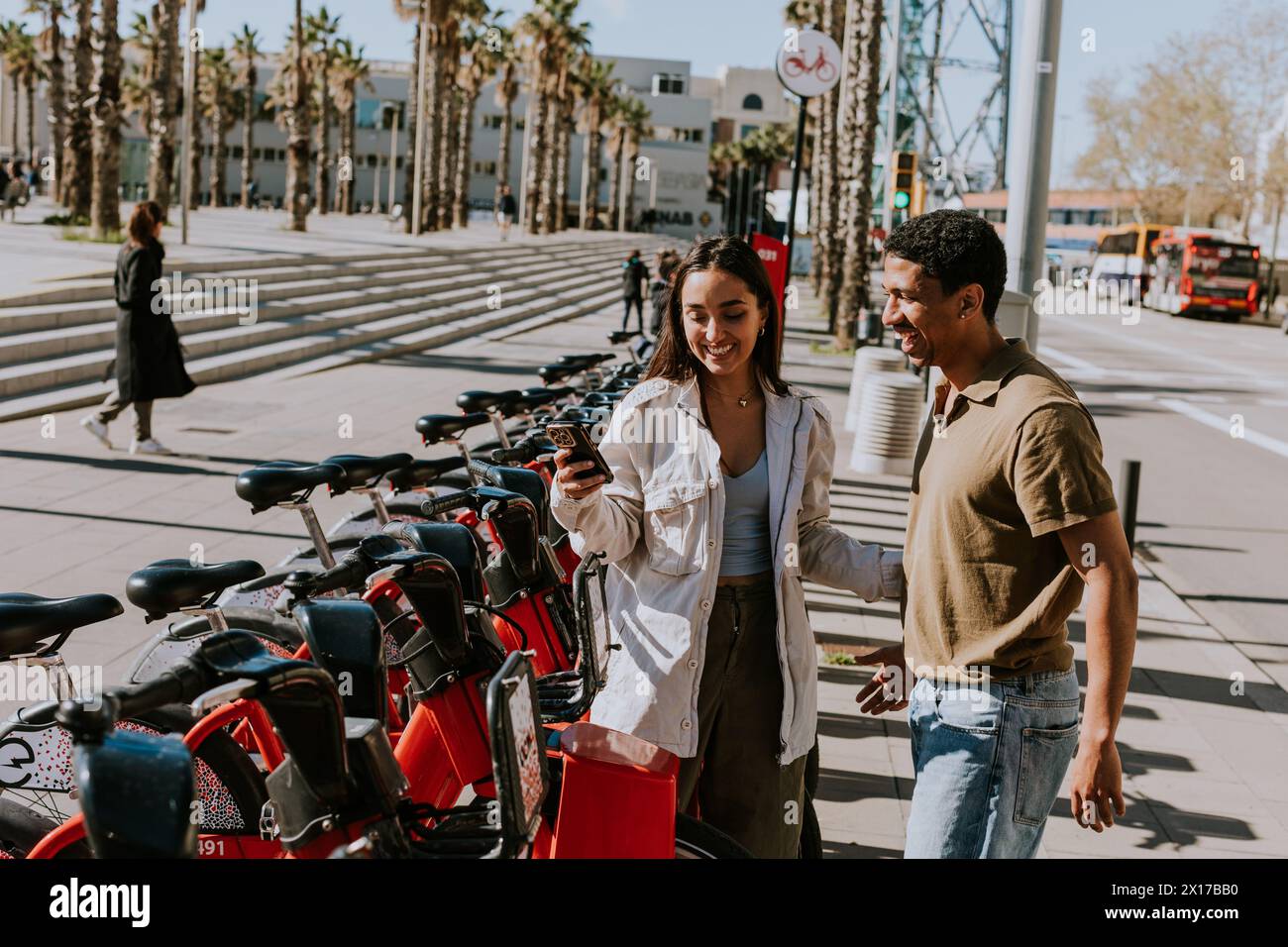 Jeune couple profitant d'une journée venteuse en choisissant des vélos d'une station de location à Barcelone. Banque D'Images