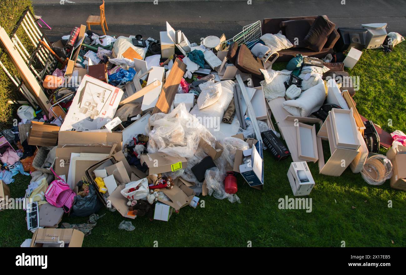 Beaucoup de déchets dans une ville près de la haus. Grandes ordures avec vieux meubles en bois, jouets, boîtes, sacs en plastique dans une rue et l'herbe verte au printemps ensoleillé tra Banque D'Images