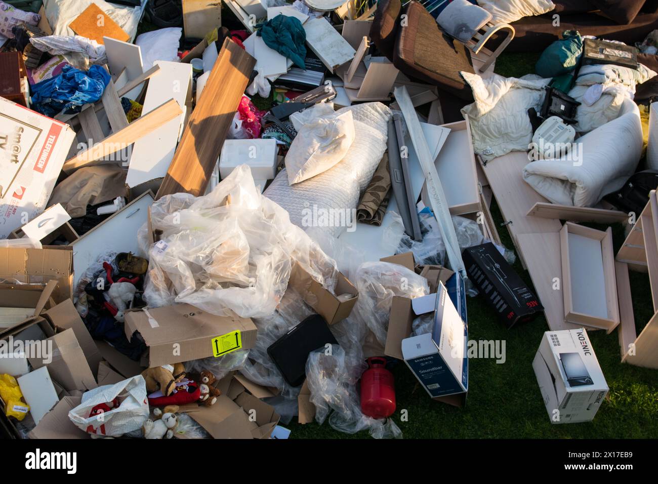 Beaucoup de déchets dans une ville près de la haus. Grandes ordures avec vieux meubles en bois, jouets, boîtes, sacs en plastique dans une rue et l'herbe verte au printemps ensoleillé tra Banque D'Images