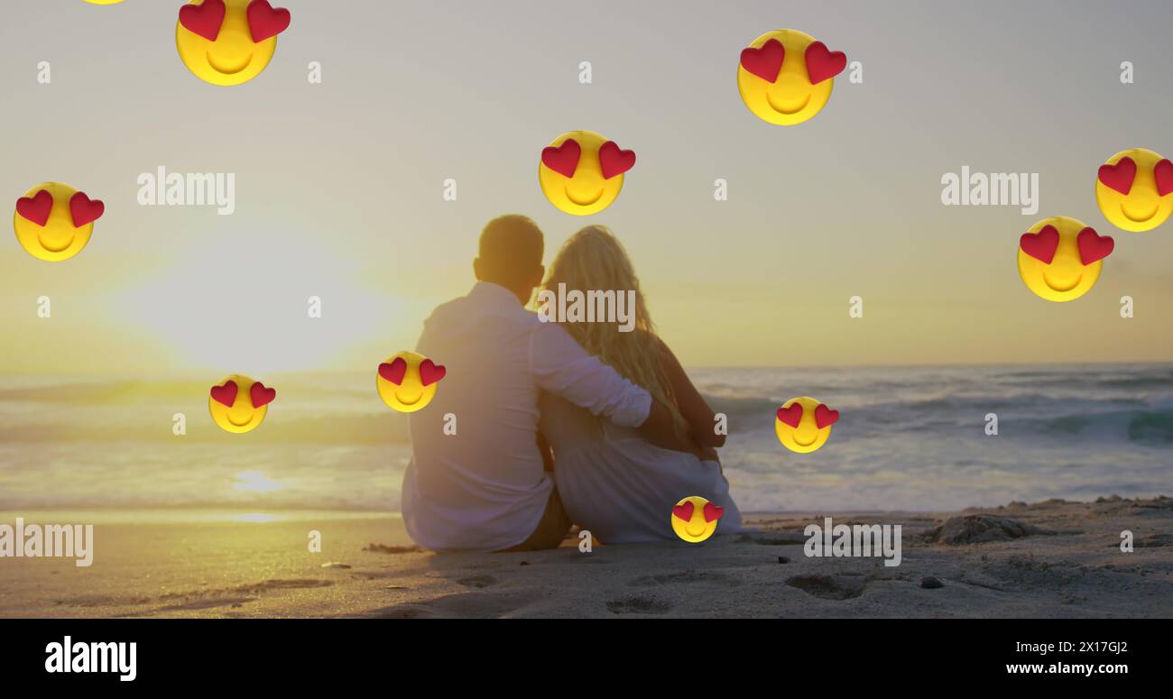 Image de multiples yeux de coeur face emoji flottant contre couple dans l'amour embrassant assis sur la plage Banque D'Images