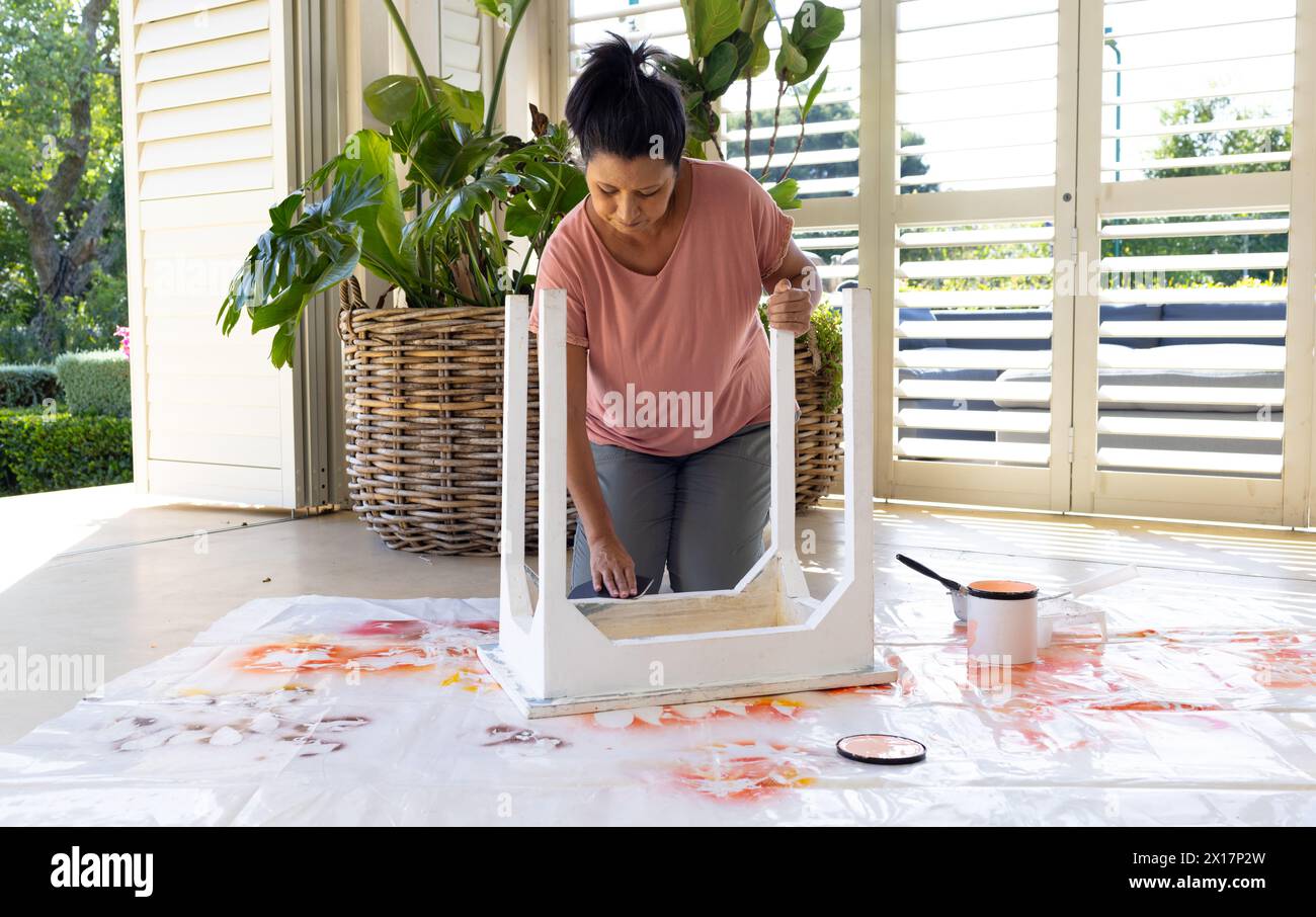 Femme biraciale mature peignant des meubles à la maison dans un projet d'upcycling Banque D'Images
