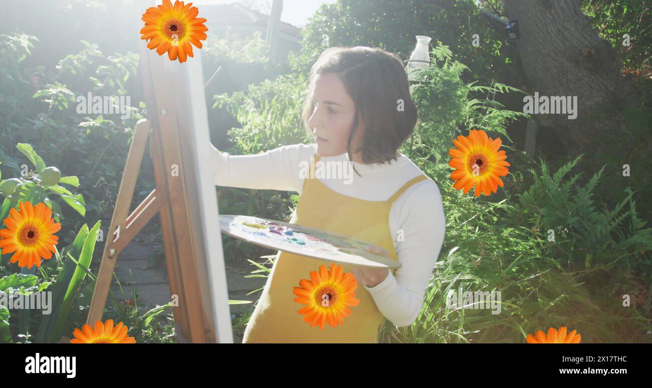 Image composite d'icônes de fleurs tombant contre la peinture d'artiste féminine caucasienne dans le jardin Banque D'Images
