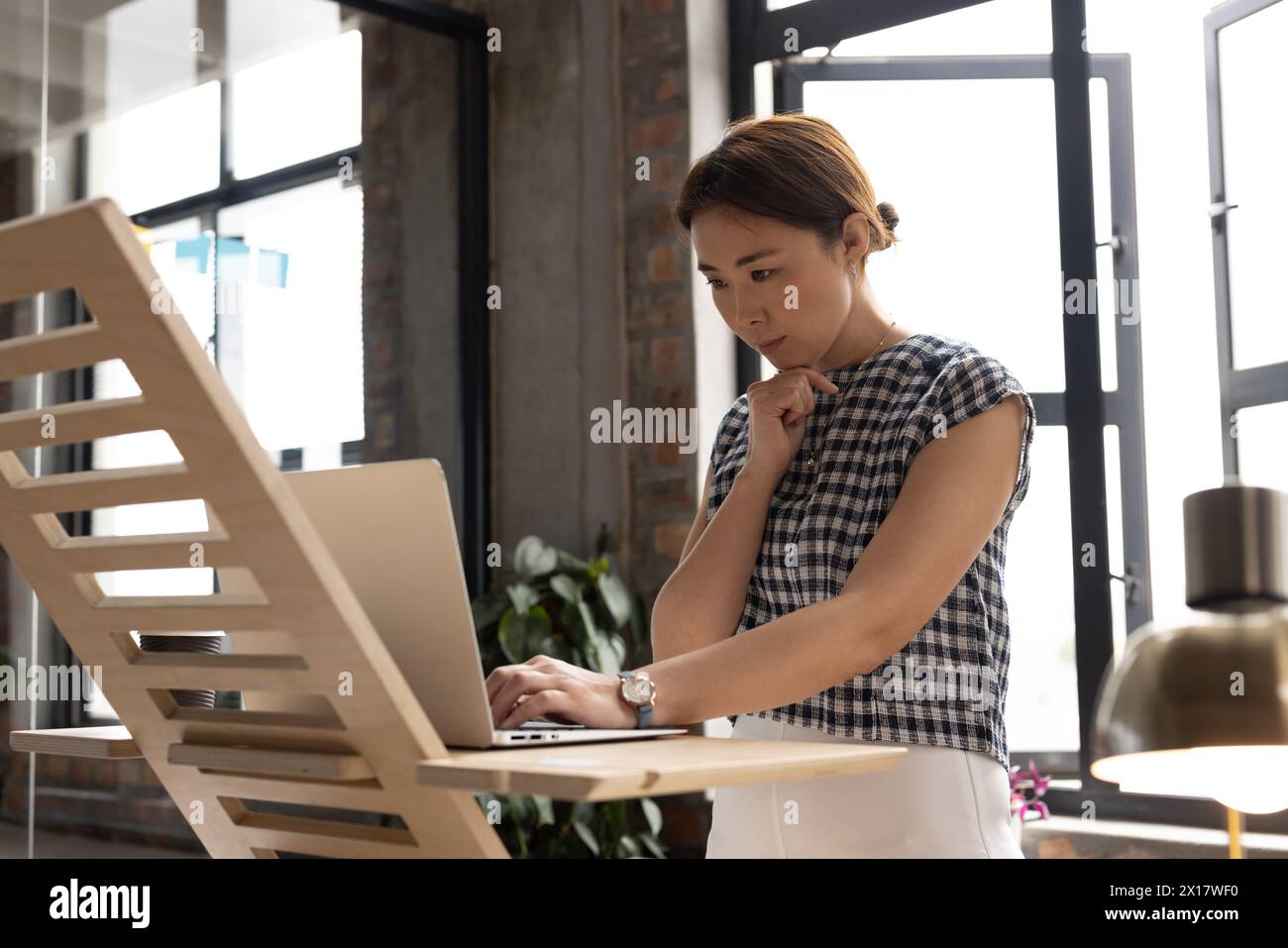 Une femme asiatique d'âge moyen debout, tapant sur un ordinateur portable dans un bureau d'affaires moderne Banque D'Images