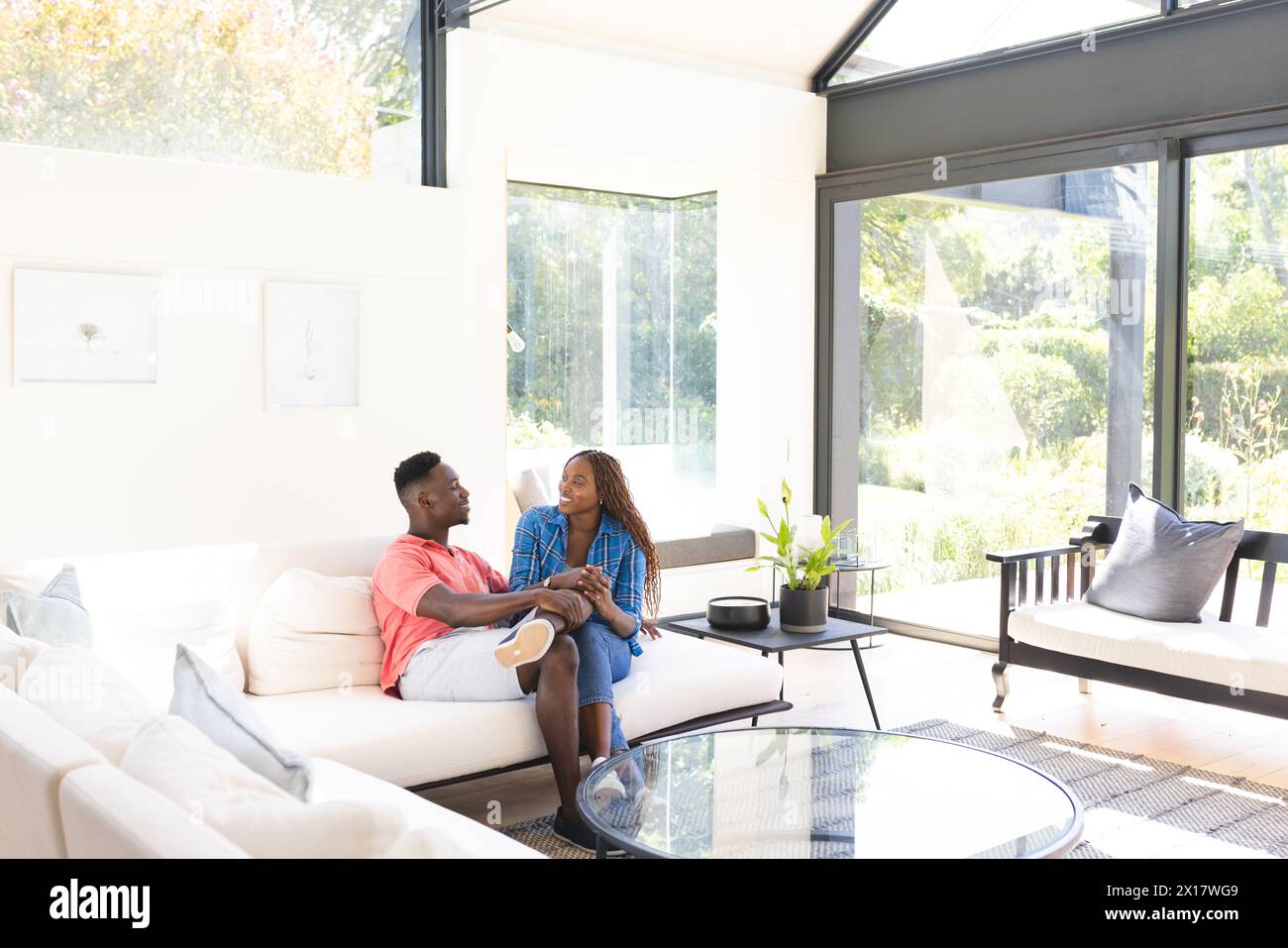 Couple afro-américain assis sur un canapé blanc, se tenant la main et parlant à la maison Banque D'Images