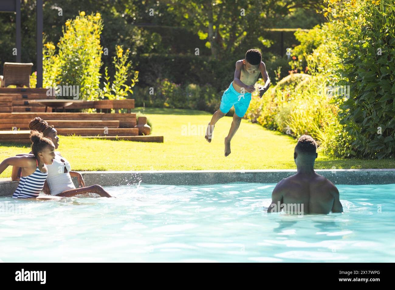 Famille afro-américaine profitant du temps de piscine à la maison, jeune garçon sautant dans l'eau Banque D'Images