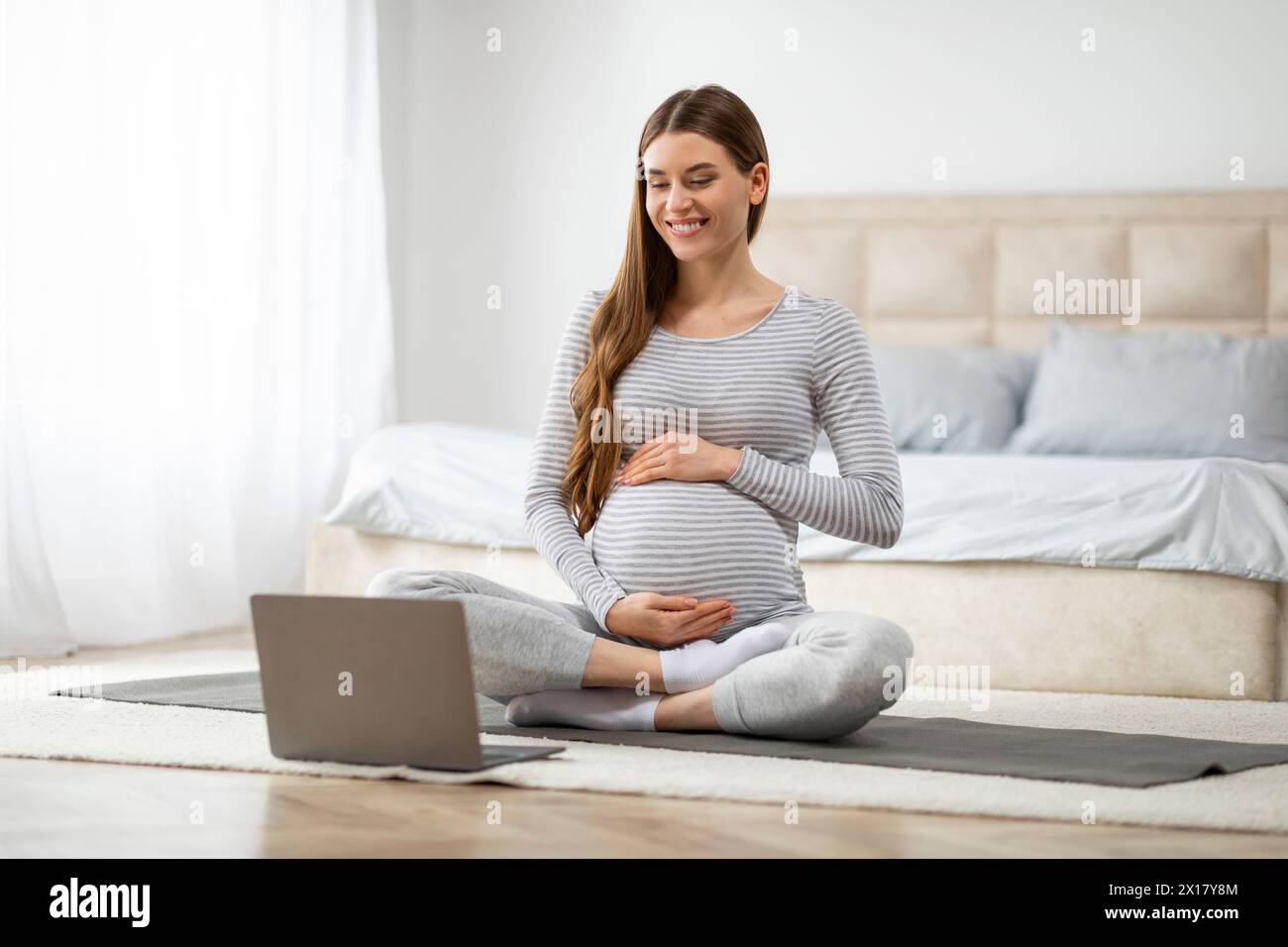 Femme enceinte pratiquant le yoga à la maison, regardant la leçon vidéo Banque D'Images
