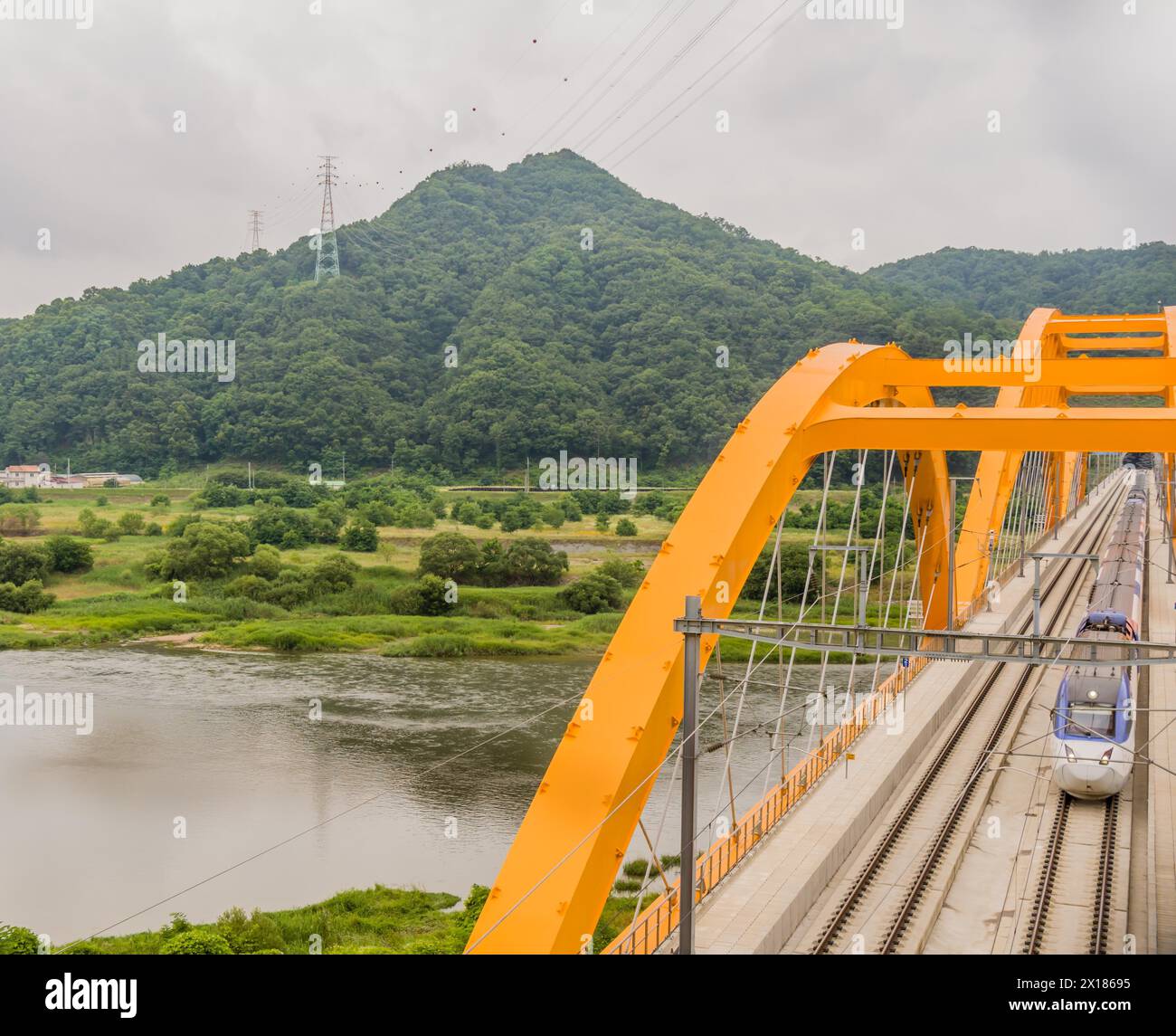 Vue de dessus d'un train traversant un pont à arc jaune au-dessus d'une rivière dans la campagne sous ciel couvert nuageux en Corée du Sud Banque D'Images