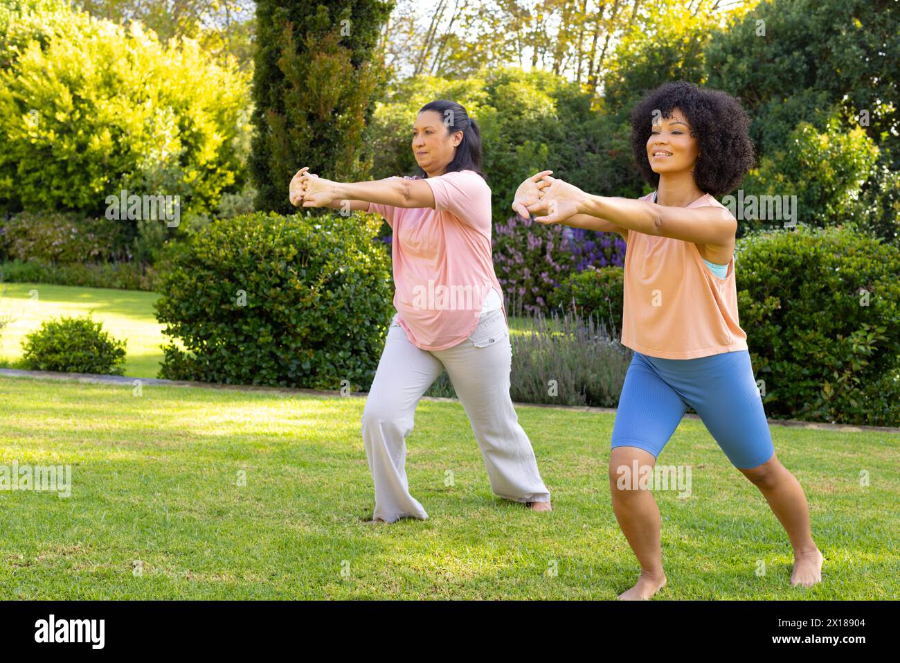 Femme biraciale mature et jeune femme biraciale exerçant dans le jardin à la maison, puis faisant du tai chi Banque D'Images
