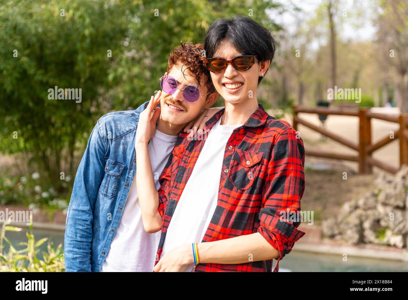 Portrait d'un couple gay multi-ethnique souriant à la caméra debout ensemble dans un parc Banque D'Images
