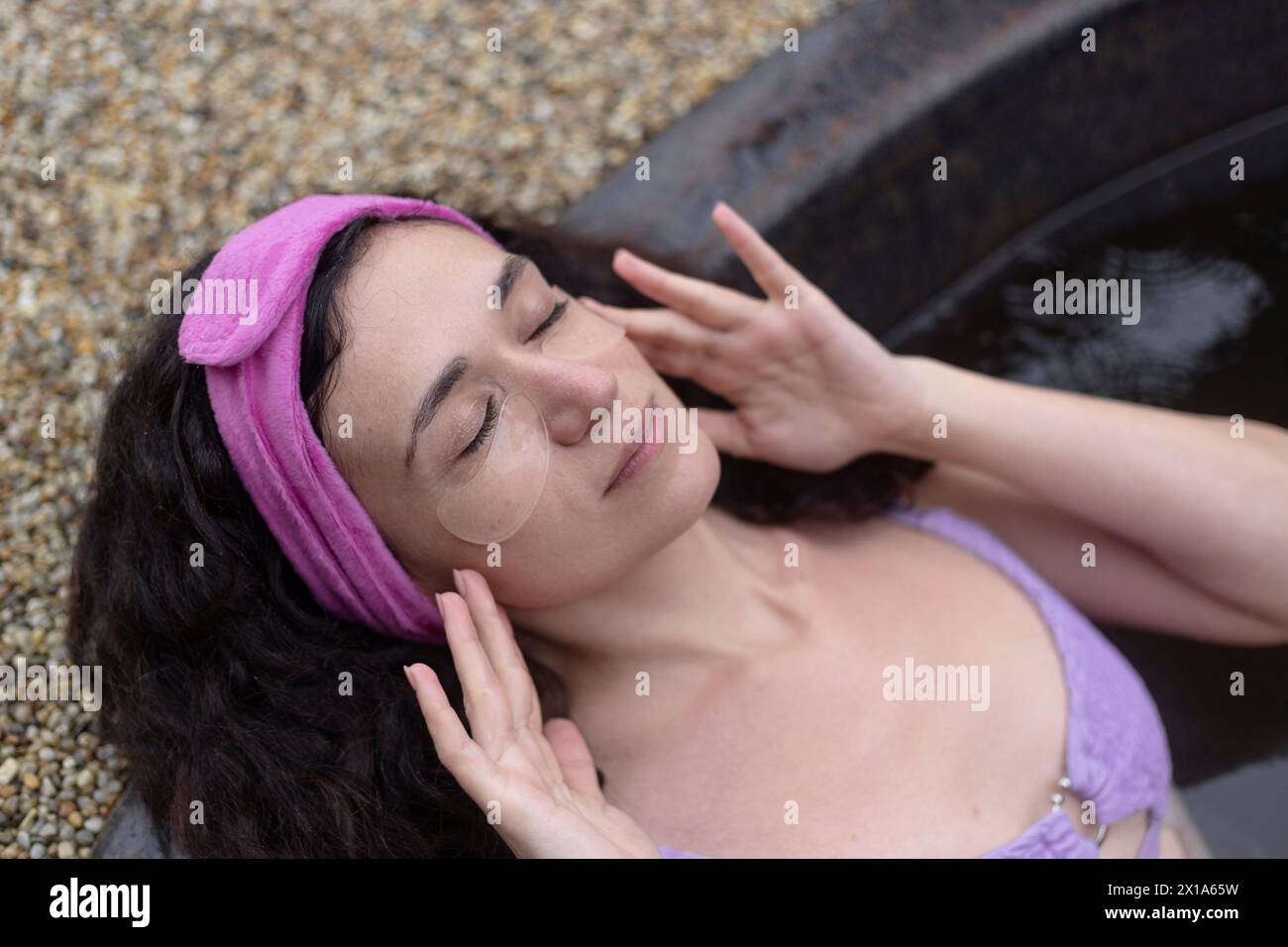 Une femme avec un bandeau rose posant inn spa avec des patchs pour les yeux Banque D'Images