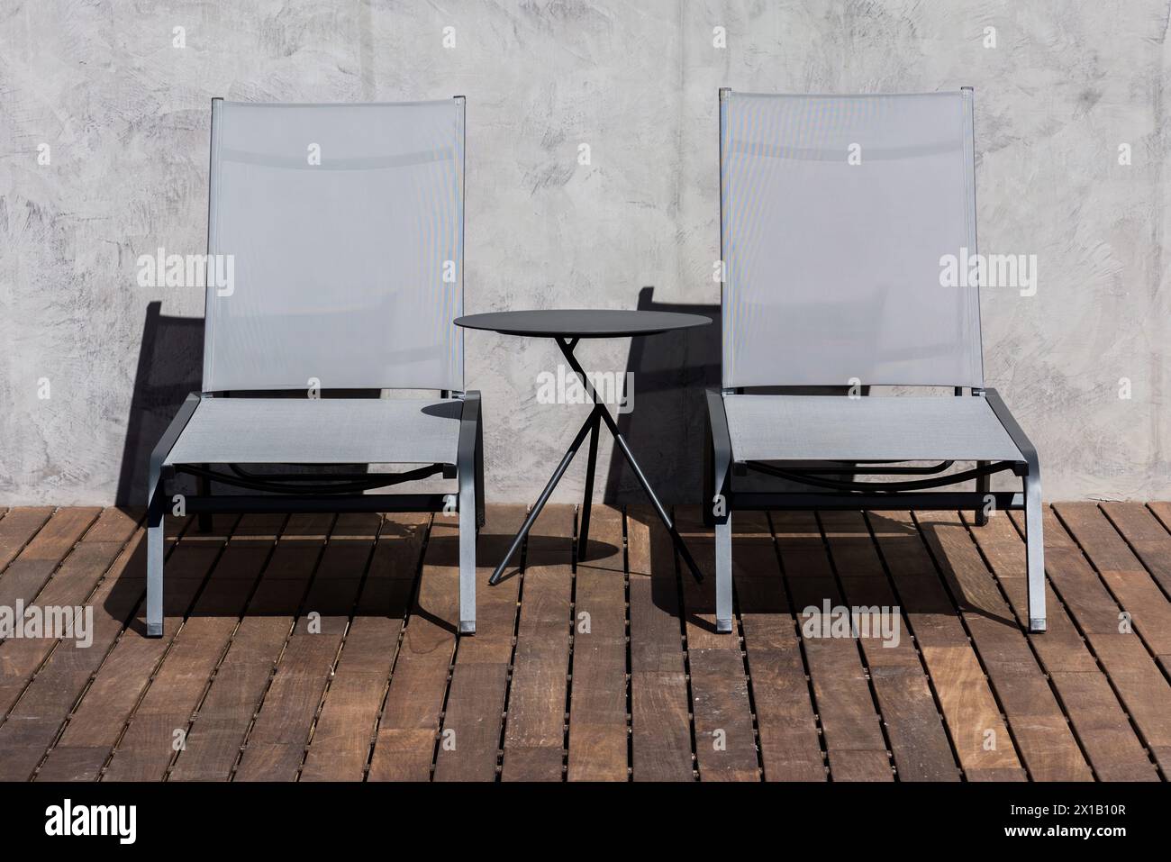Une paire de chaises longues élégantes et noires avec sièges en maille transparente sont positionnées sur une terrasse en bois, accompagnées d'une petite table d'appoint ronde Banque D'Images