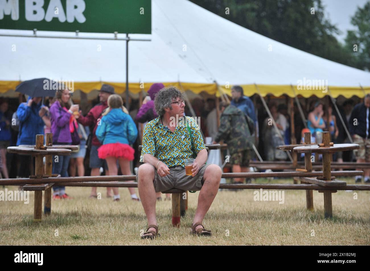 Un homme profite de sa bière malgré la pluie pendant le festival WOMAD 2013, qui se tient à Charlton Park, Wiltshire. Banque D'Images