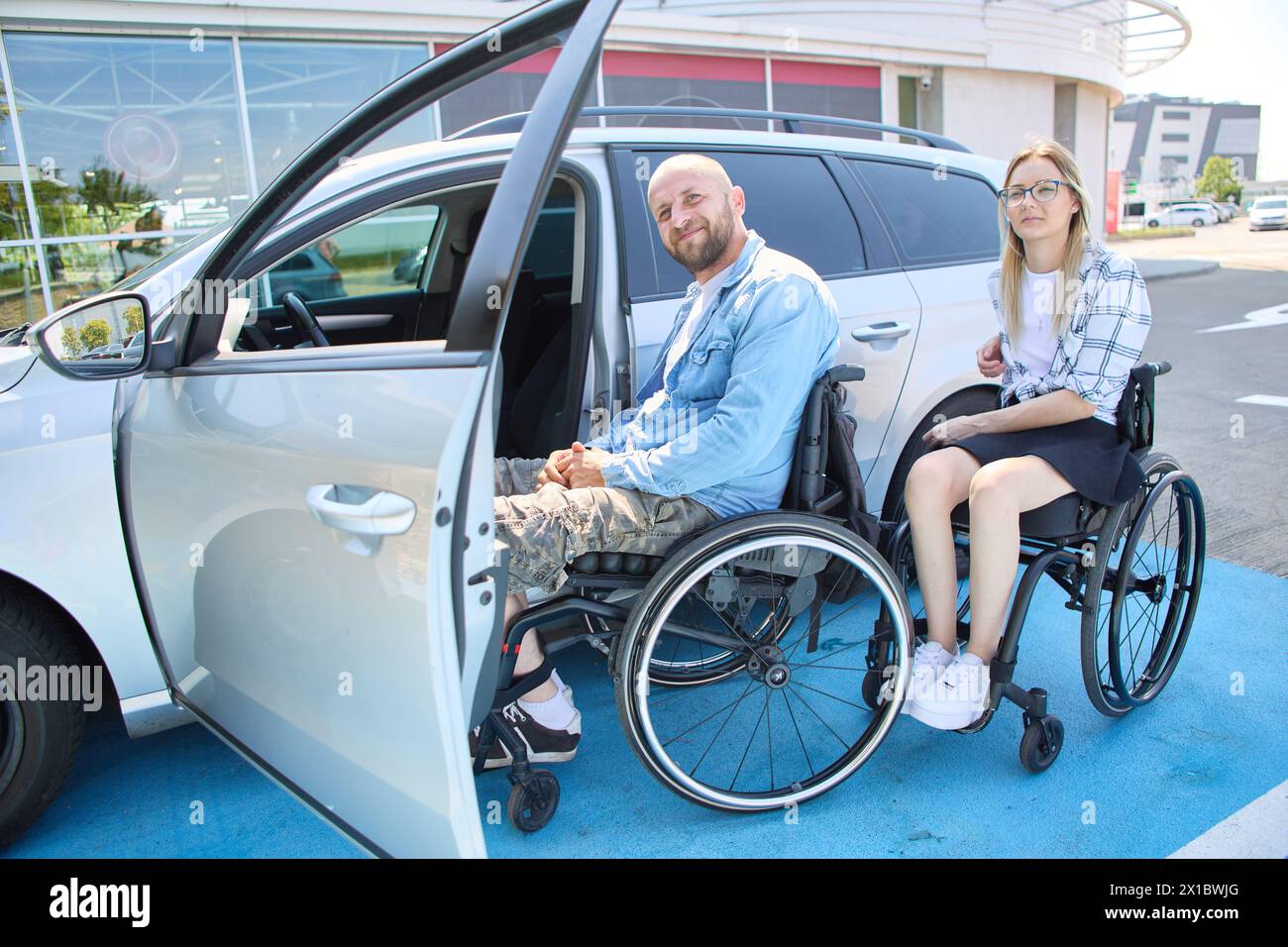 Un homme et une femme qui utilisent des fauteuils roulants sont photographiés près d’une voiture accessible, démontrant mobilité et indépendance dans un environnement urbain. Banque D'Images Un homme et une femme qui utilisent des fauteuils roulants sont photographiés près d’une voiture accessible, démontrant mobilité et indépendance dans un environnement urbain. Banque D'Images
