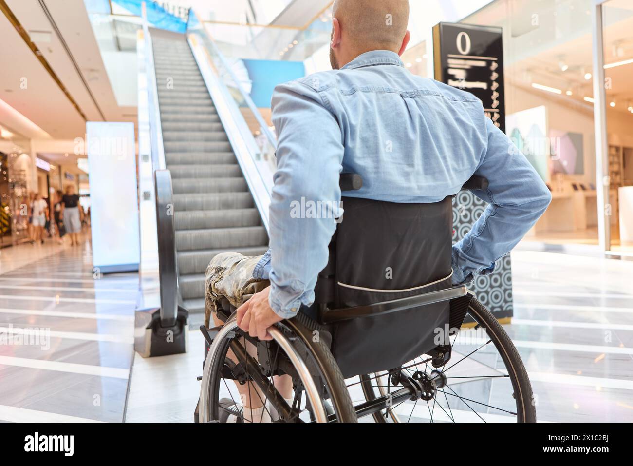 L'image capture un homme en fauteuil roulant dans un centre commercial, soulignant l'importance des espaces inclusifs et la vie quotidienne des personnes qui utilisent la roue Banque D'Images