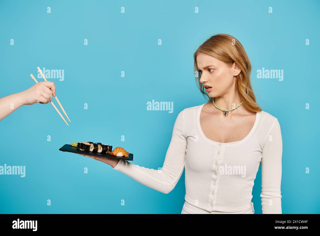 Une belle femme blonde tient délicatement une assiette de sushis, mettant en valeur l'art de la cuisine japonaise, les baguettes. Banque D'Images