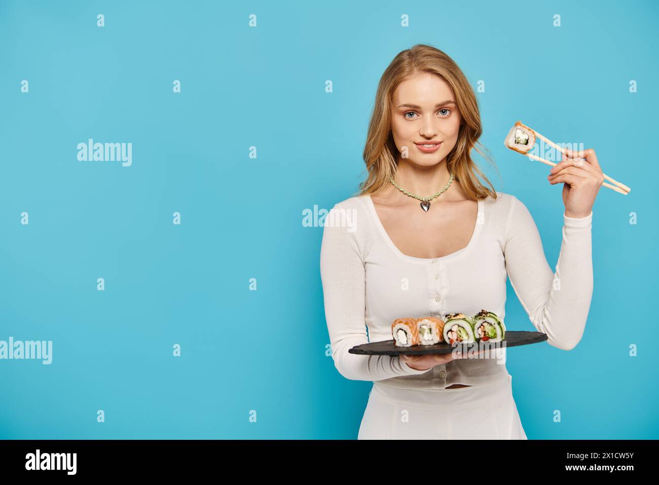 Une belle femme aux cheveux blonds tient délicatement une assiette remplie de délicieux rouleaux de sushi. Banque D'Images