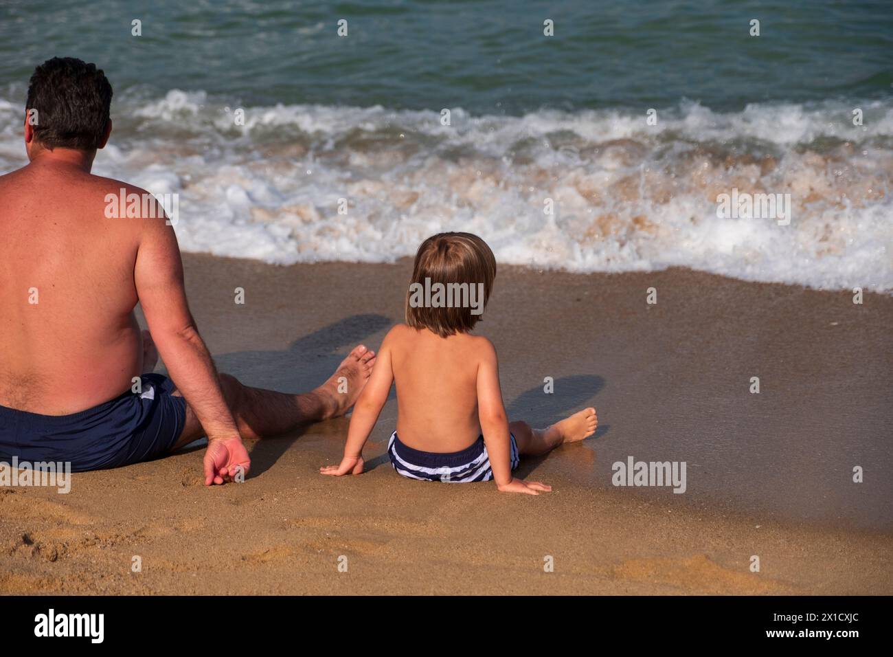 Un père et son fils assis sur la plage de sable doré profitant des vagues de la mer et de la vue sur la mer noire. Banque D'Images