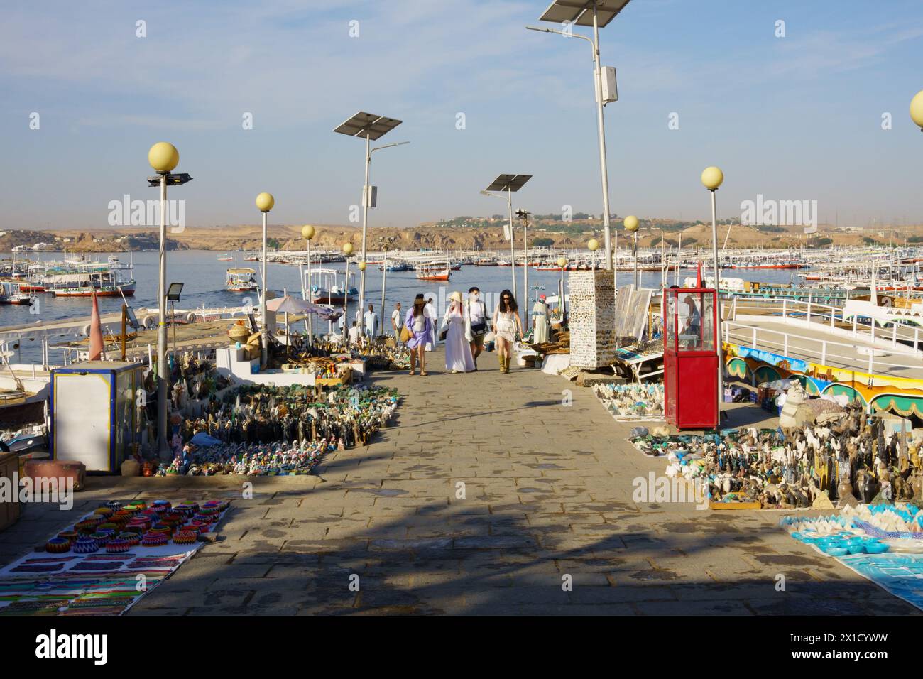 Touristes marchant jusqu'à la cale de la marina Philae Temple des bateaux touristiques, passé des souvenirs sur le sol. Assouan, Égypte Banque D'Images