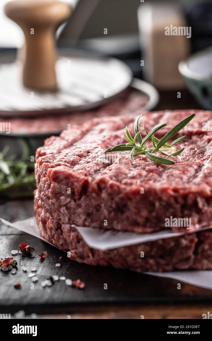 Patties de bœuf haché cru frais avec sel de romarin et poivre préparées sous forme de viande sur une planche à découper. Banque D'Images