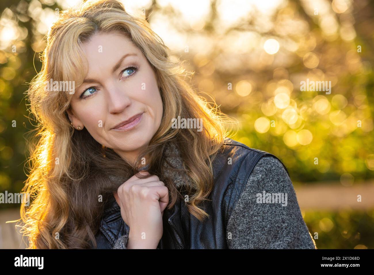 Belle femme heureuse souriante d'âge moyen à l'extérieur du dos éclairée par le soleil chaud au coucher du soleil ou au lever du soleil Banque D'Images