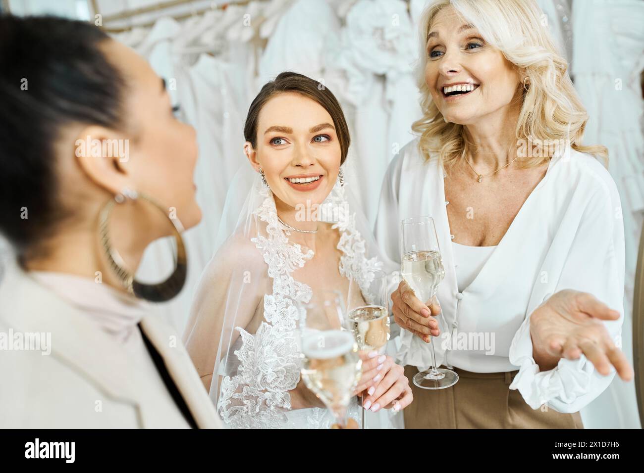 Une jeune mariée dans une robe de mariée, sa mère d'âge moyen, et une demoiselle d'honneur dans un salon de mariée, tenant des verres à vin. Banque D'Images