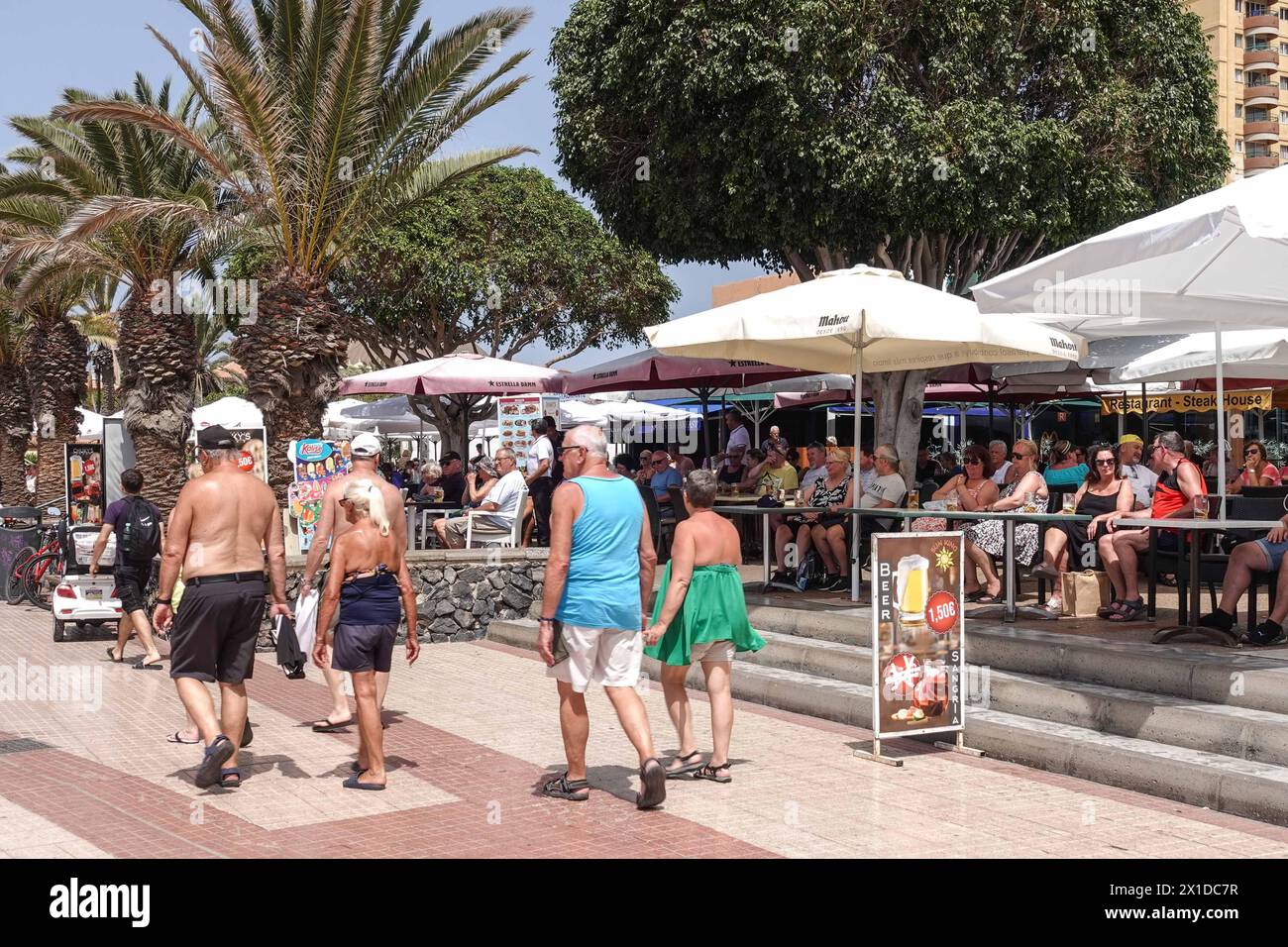 Los Cristianos, Tenerife, 16 avril 2024 - les touristes boivent dans des bars anglais de front de mer où une pinte de bière est 1.50E. - Les touristes passent devant des affiches anti-touristiques le long du front de mer à Los Cristianos. L'affiche dit que "les îles Canaries ont une limite" les panneaux jaunes annoncent la manifestation anti-touristique du samedi 20 avril. À Santa Cruz de Tenerife. Le stationnement est également un gros problème dans la région car des hordes de visiteurs remplissent des milliers de places, causant un mal de tête pour les résidents et les visiteurs. Crédit : arrêtez Press Media/Alamy Live News Banque D'Images