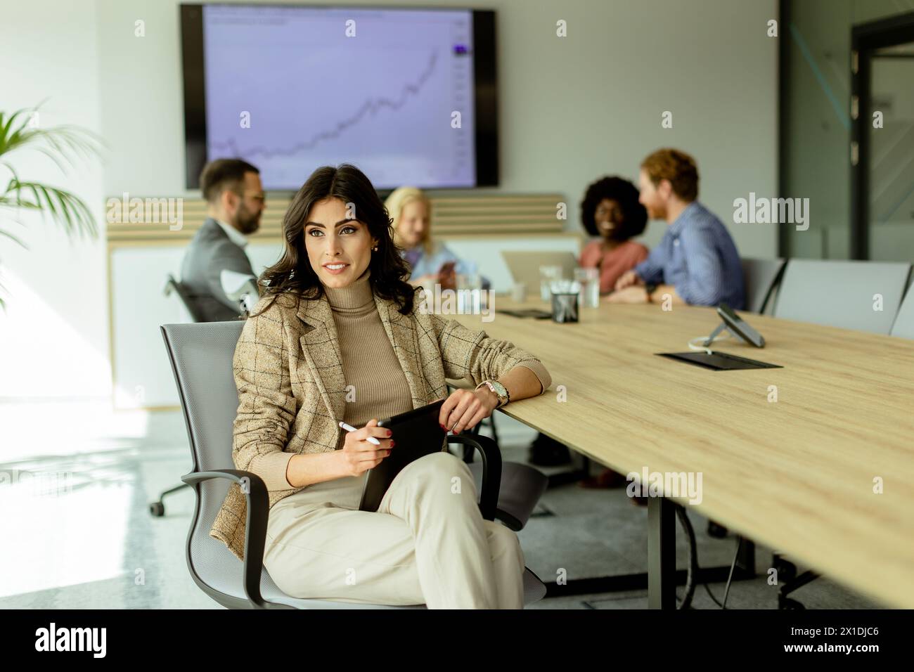 Une femme d'affaires profondément dans la pensée tandis que les collègues discutent des stratégies en arrière-plan. Banque D'Images