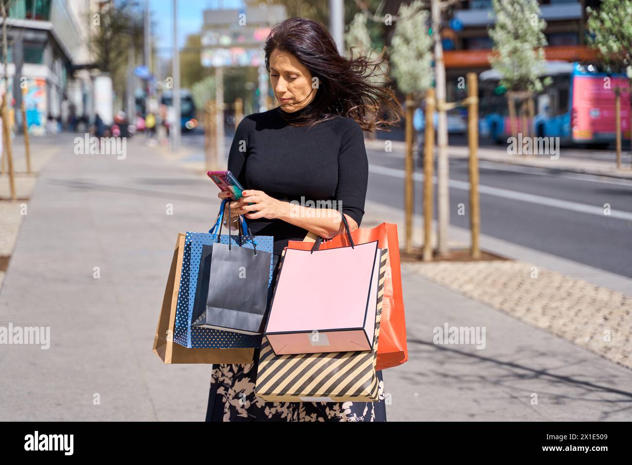 femme d'âge moyen avec des sacs à provisions à l'aide de son téléphone intelligent Banque D'Images