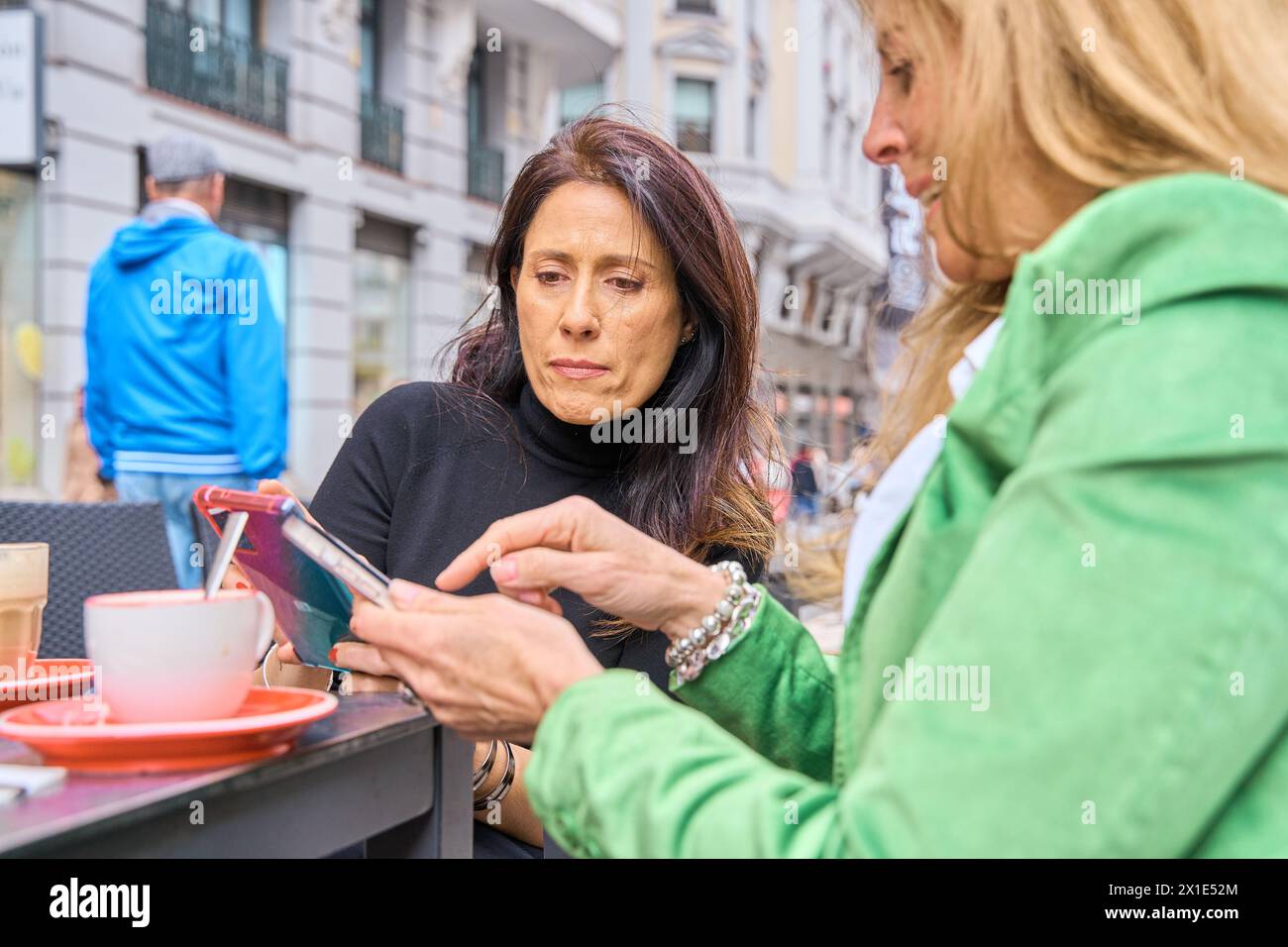 Deux filles dans un café, souriant, bavardant, buvant du café, regardant un smartphone Banque D'Images